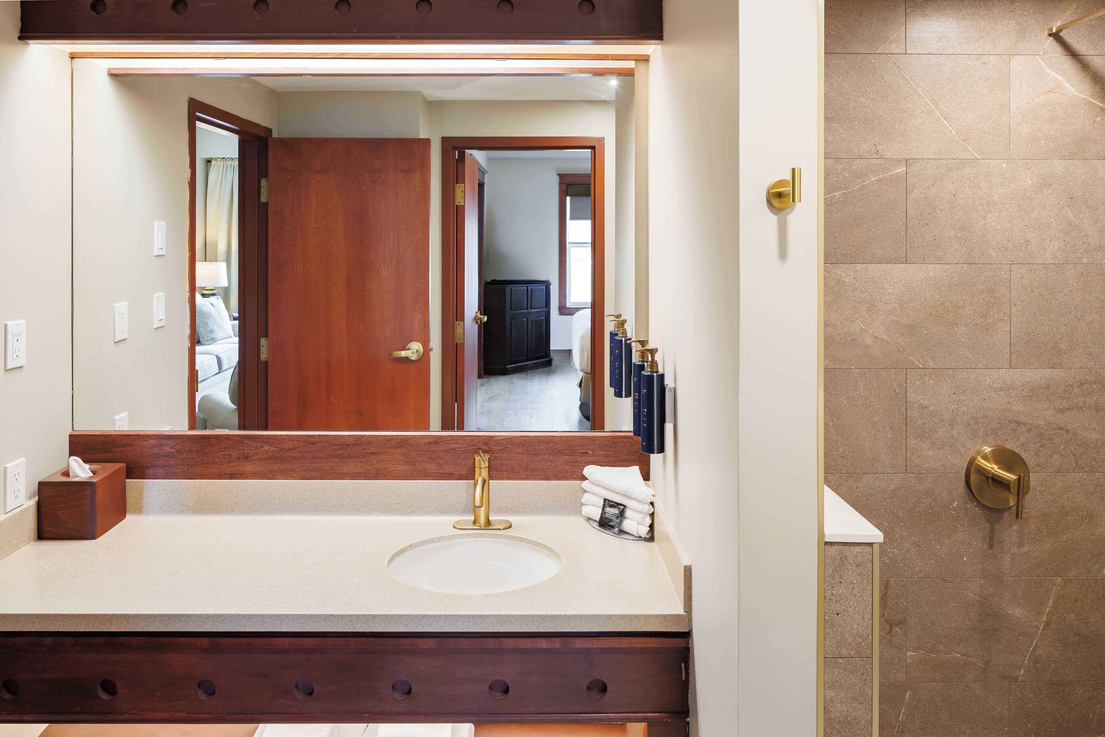 A bathroom with a large mirror, a sink with a gold faucet, and a shower area.