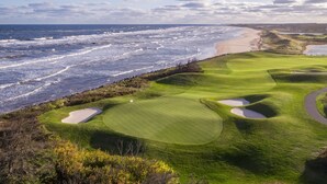 Un parcours de golf situé sur la côte, avec des drapeaux, des bunkers de sable et une vue sur l’océan.