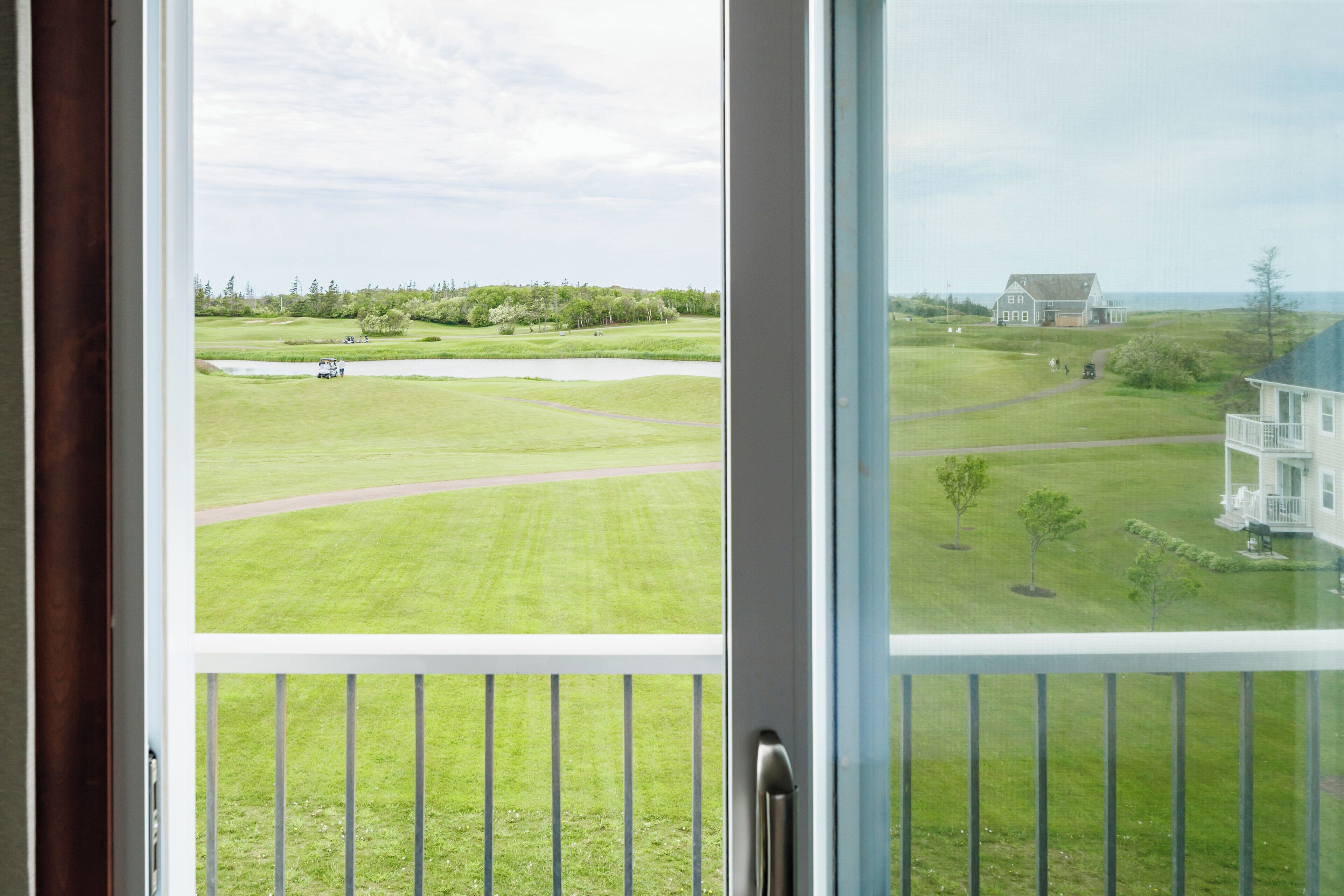 Vista desde una ventana sobre un campo de golf, con una casa a lo lejos.