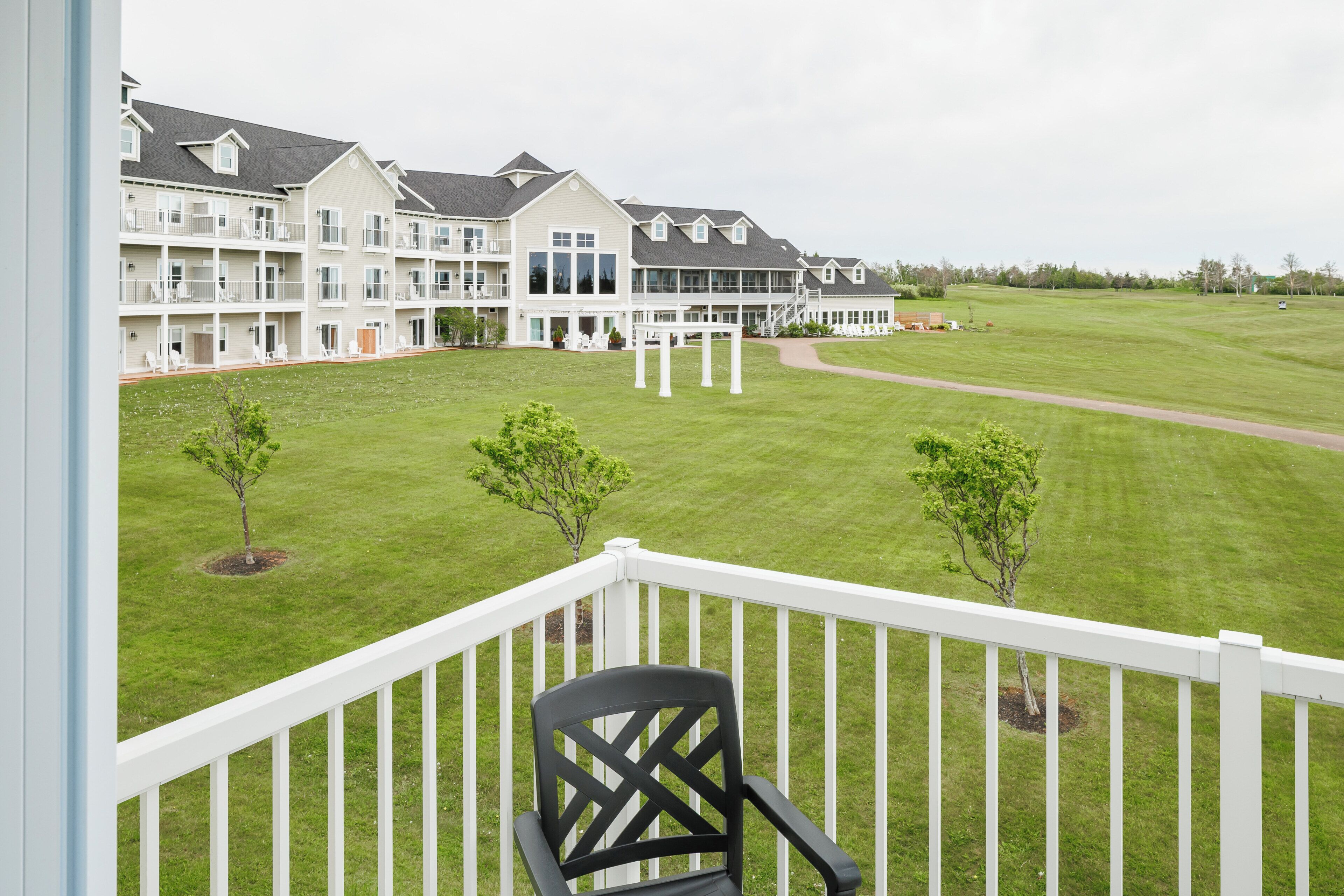 A balcony with a view of a multi-story building with a lawn and trees.