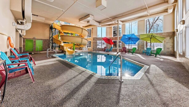 Una piscina interior con tobogán, sillas de descanso y sombrillas.