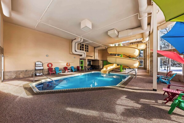 An indoor swimming pool with a slide, surrounded by colorful chairs and a sunshade. - Wingate by Wyndham Calgary (Calgary)