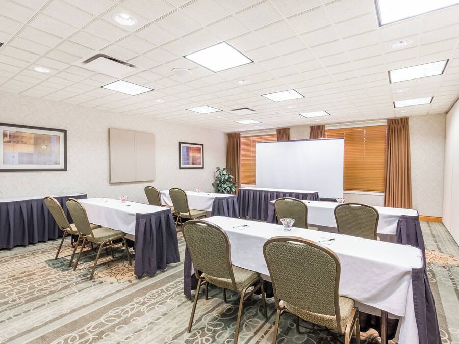 Sala de conferências com mesas, cadeiras, quadro branco e tela de projeção.