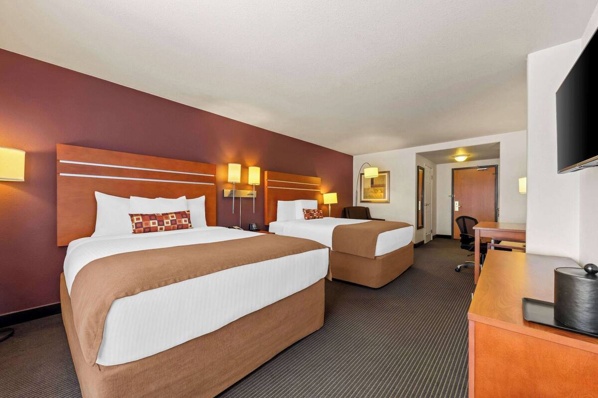 A hotel room with two beds, a desk, and a TV.