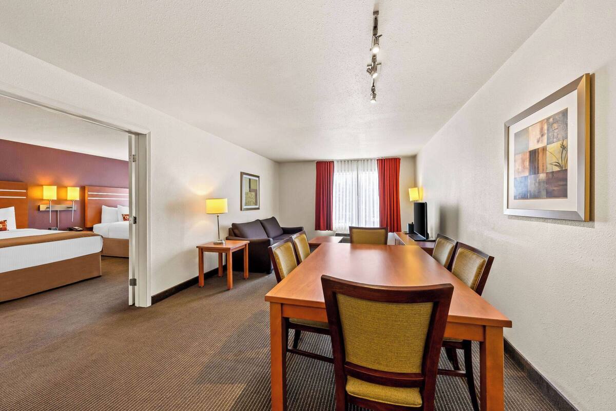 A hotel room with a bed, a desk, a dining table with chairs, a sofa, and a television.