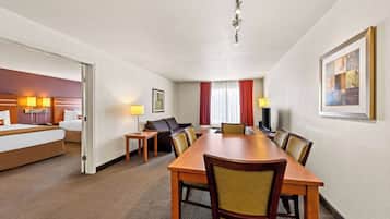 Habitación de hotel con cama, escritorio, mesa de comedor con sillas, sofá y televisión.