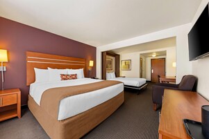 Habitación de hotel con dos camas, un escritorio, una silla, un televisor y una puerta que da a un comedor.