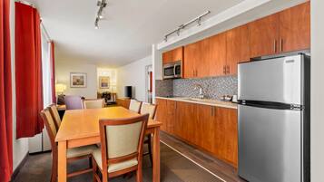 Una cocina moderna con armarios de madera, un refrigerador de acero inoxidable y una zona de comedor con mesa y sillas de madera.