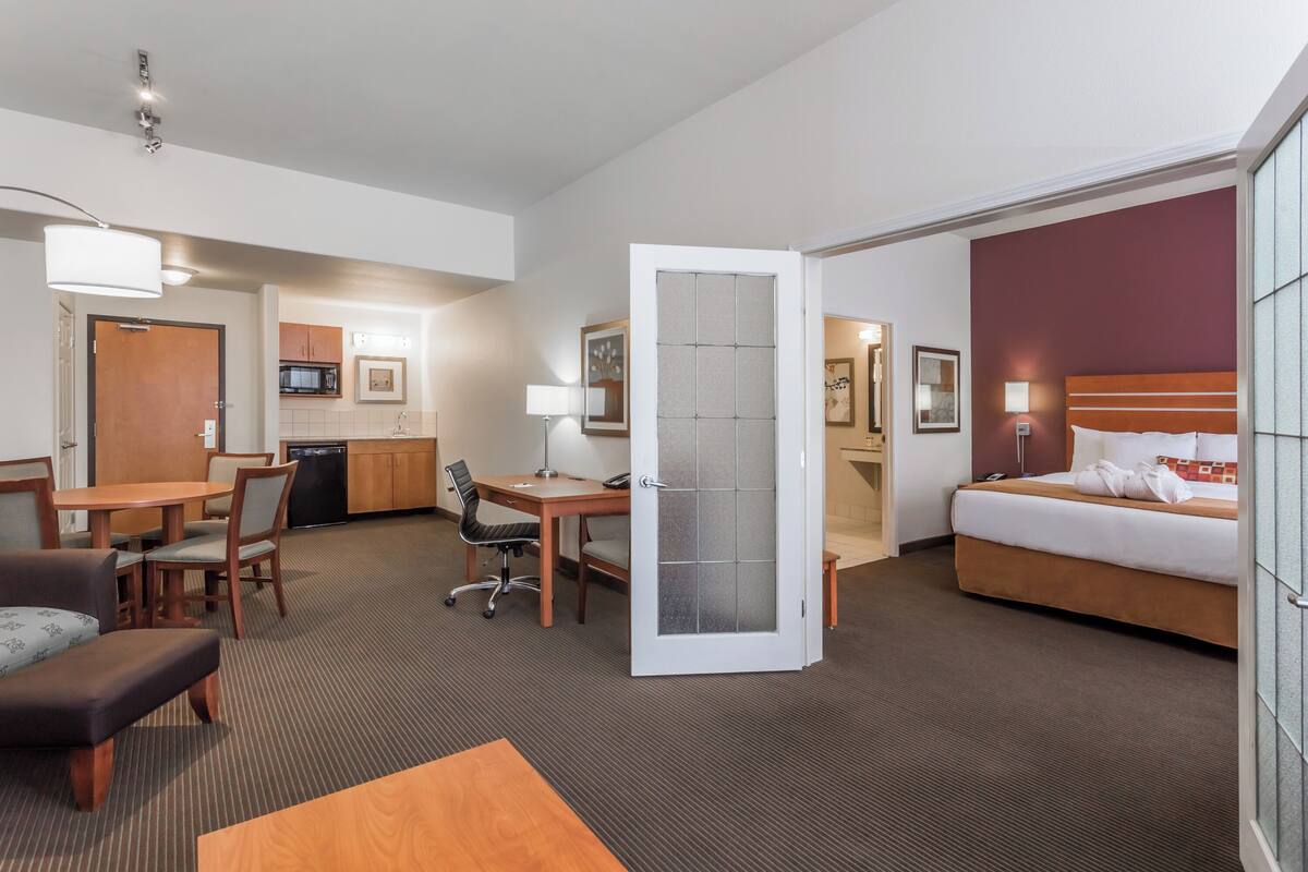 A hotel room with a bed, a desk, a chair, a sofa, and a kitchenette area.