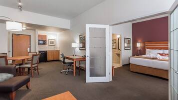 A hotel room with a bed, a desk, a chair, a sofa, and a kitchenette area.