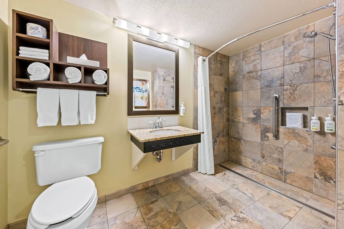 A bathroom with a toilet, sink, mirror, shower, and towel rack.
