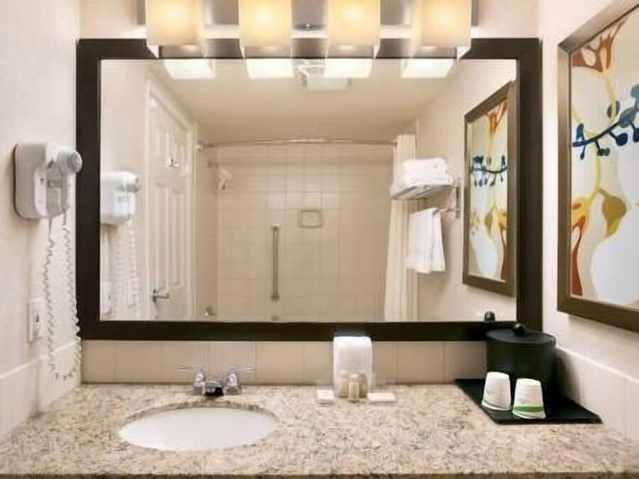 A bathroom with a large mirror, a sink, a towel rack, and a shower.