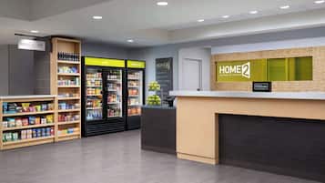 Un hall d’hôtel avec un comptoir d’accueil, une enseigne « HOME 2 », une enseigne « Hilton Honors » et un réfrigérateur à boissons « très froid ».