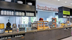 Un espace pour le petit-déjeuner avec un buffet où les clients peuvent se servir eux-mêmes, comprenant des tasses, des couverts et une machine à café.
