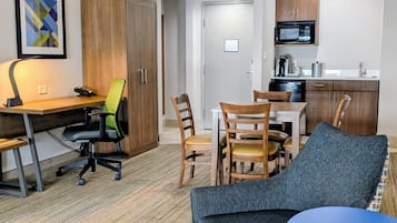 Un espacio habitable compacto con escritorio, silla de oficina, mesa de comedor y sillas. Se ve un microondas y una cafetera en la kitchenette.