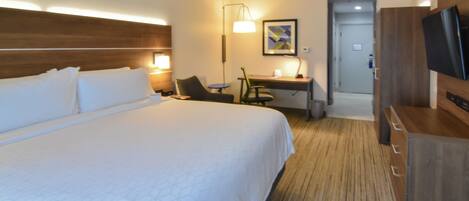 A hotel room with a large bed, a desk, a chair, a television, and a lamp.
