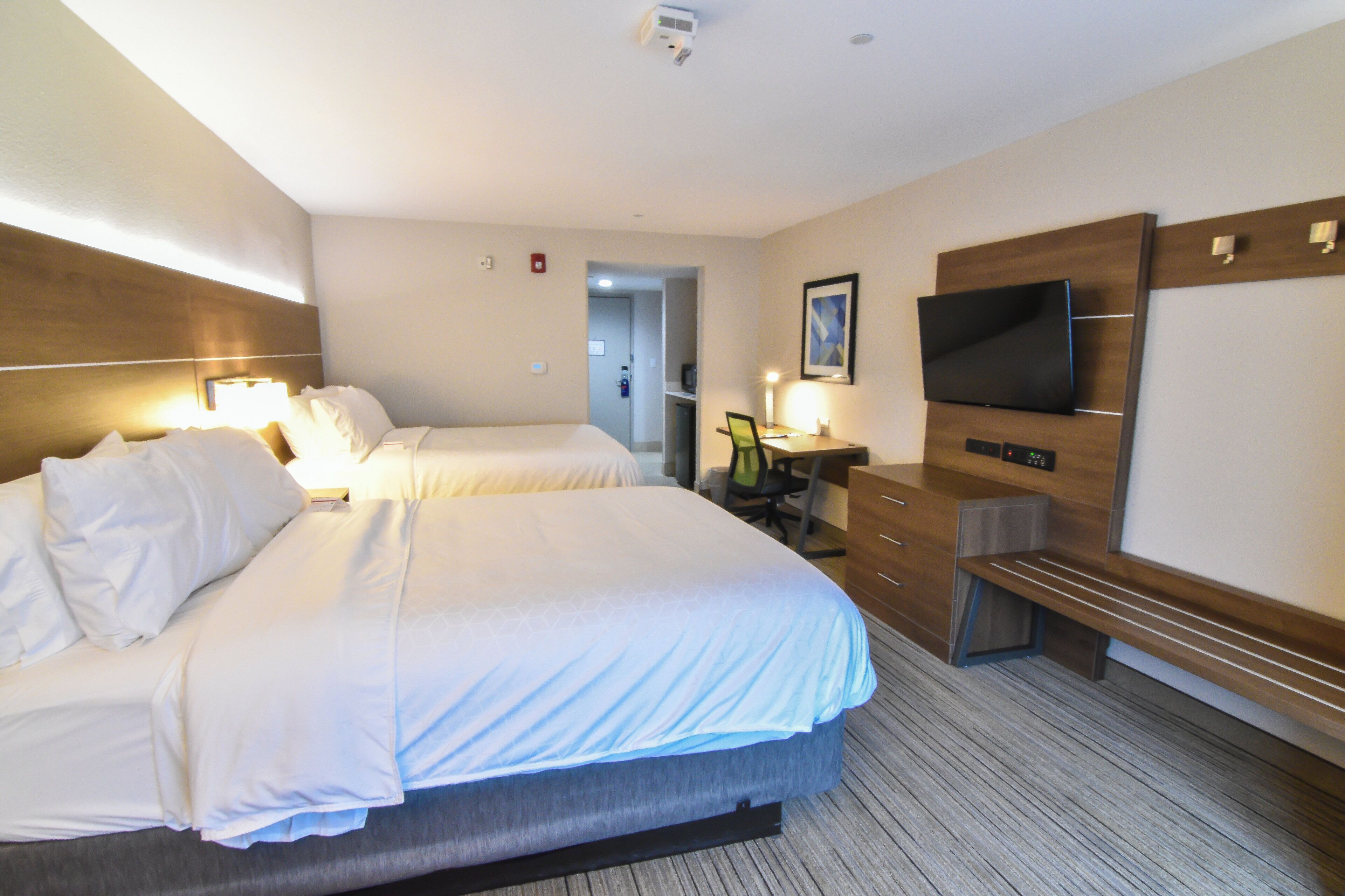 A hotel room with two beds, a desk, a chair, a television, and a door leading to a bathroom.