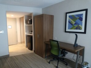 Une chambre d’hôtel avec un bureau en bois, une chaise de bureau verte, un tableau abstrait encadré et une armoire.