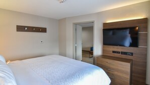 Une chambre d’hôtel avec un grand lit, un téléviseur à écran plat fixé au mur et une commode en bois avec des tiroirs.