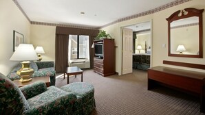 A hotel room with a sofa, a small table, a TV stand, a mirror, and a door leading to another room. - Holiday Inn Express & Suites Indianapolis Northwest by IHG (Indianapolis)