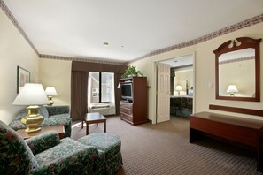 Une chambre d’hôtel avec un canapé, une petite table, un meuble pour la télévision, un miroir et une porte donnant sur une autre pièce.
