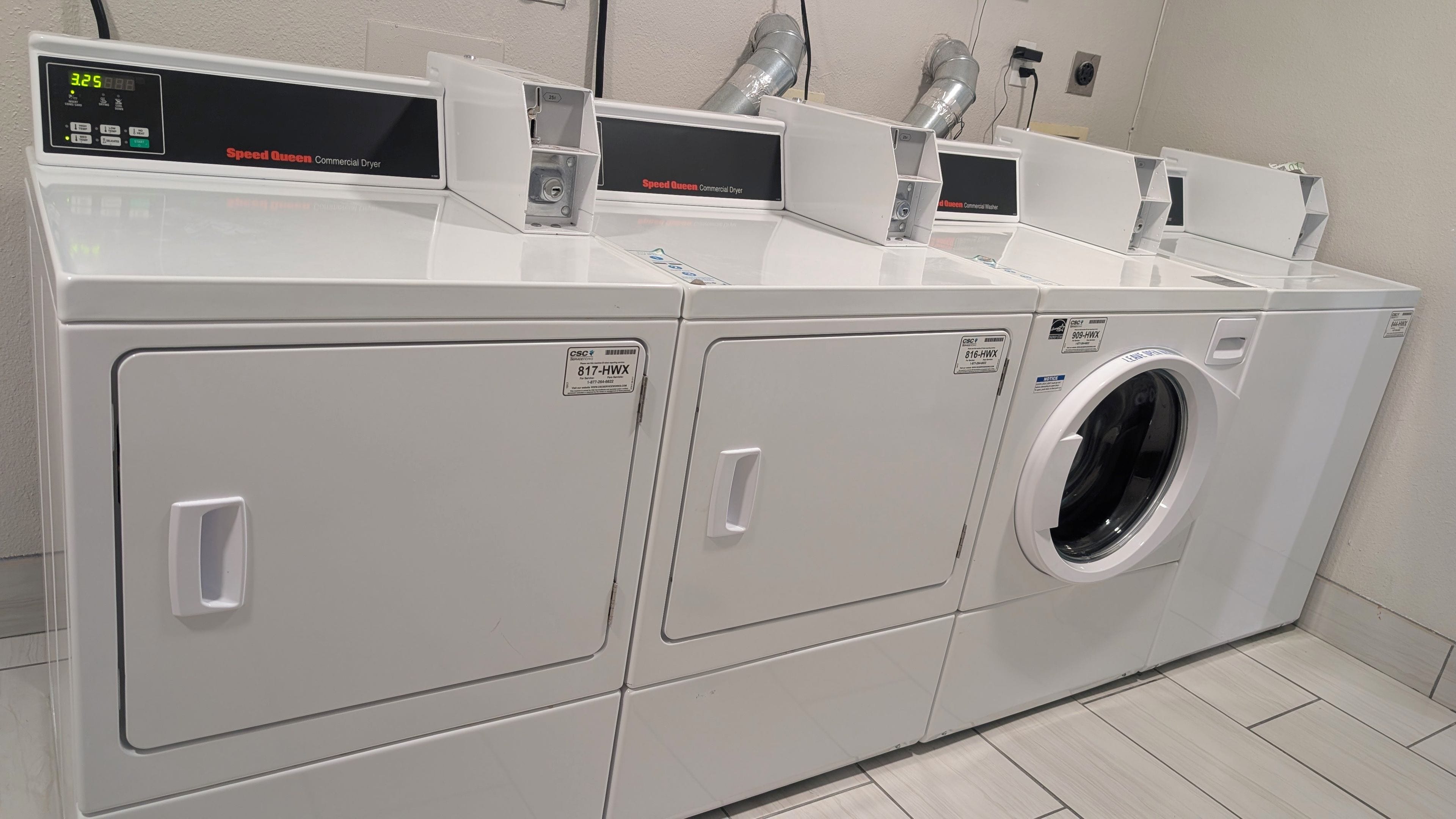 A row of Speed Queen commercial dryers with control panels, located in a laundry facility.