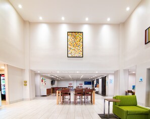 Experience the hotel's inviting lobby, featuring a central dining area, comfortable seating, and a vibrant artwork on display.