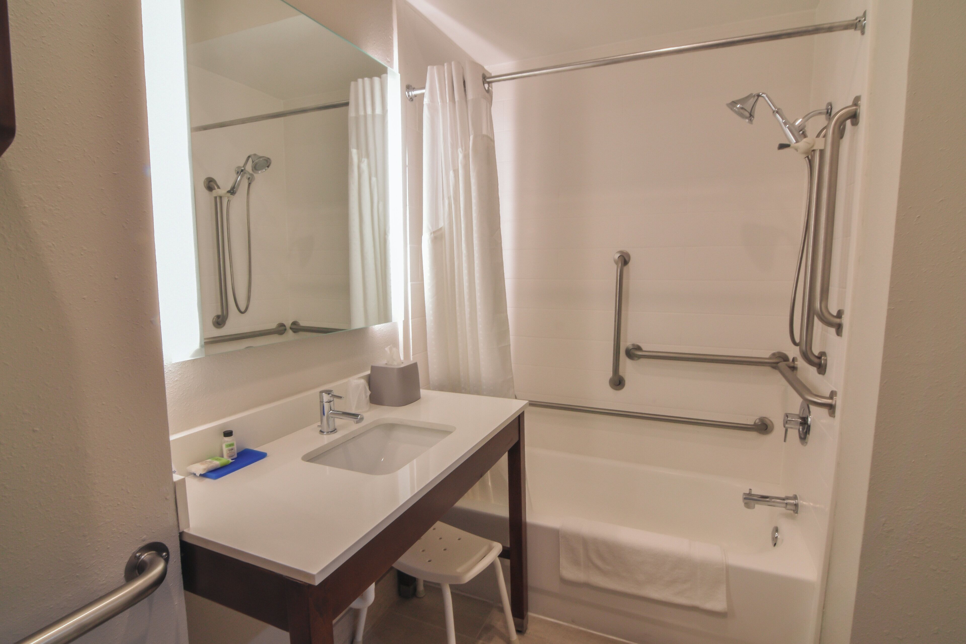 A bathroom with a bathtub, a shower with grab bars, a sink with a mirror, and a towel rack.
