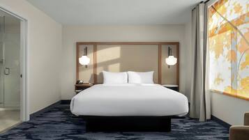 A hotel room with a large bed, a nightstand, a lamp, a window with curtains, and a view of autumn leaves.