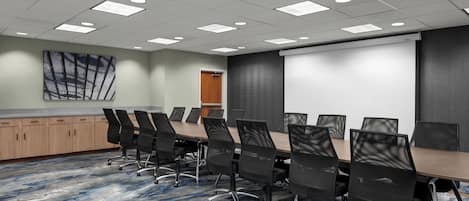 A conference room with a long table, black chairs, a projector screen, and a carpeted floor.