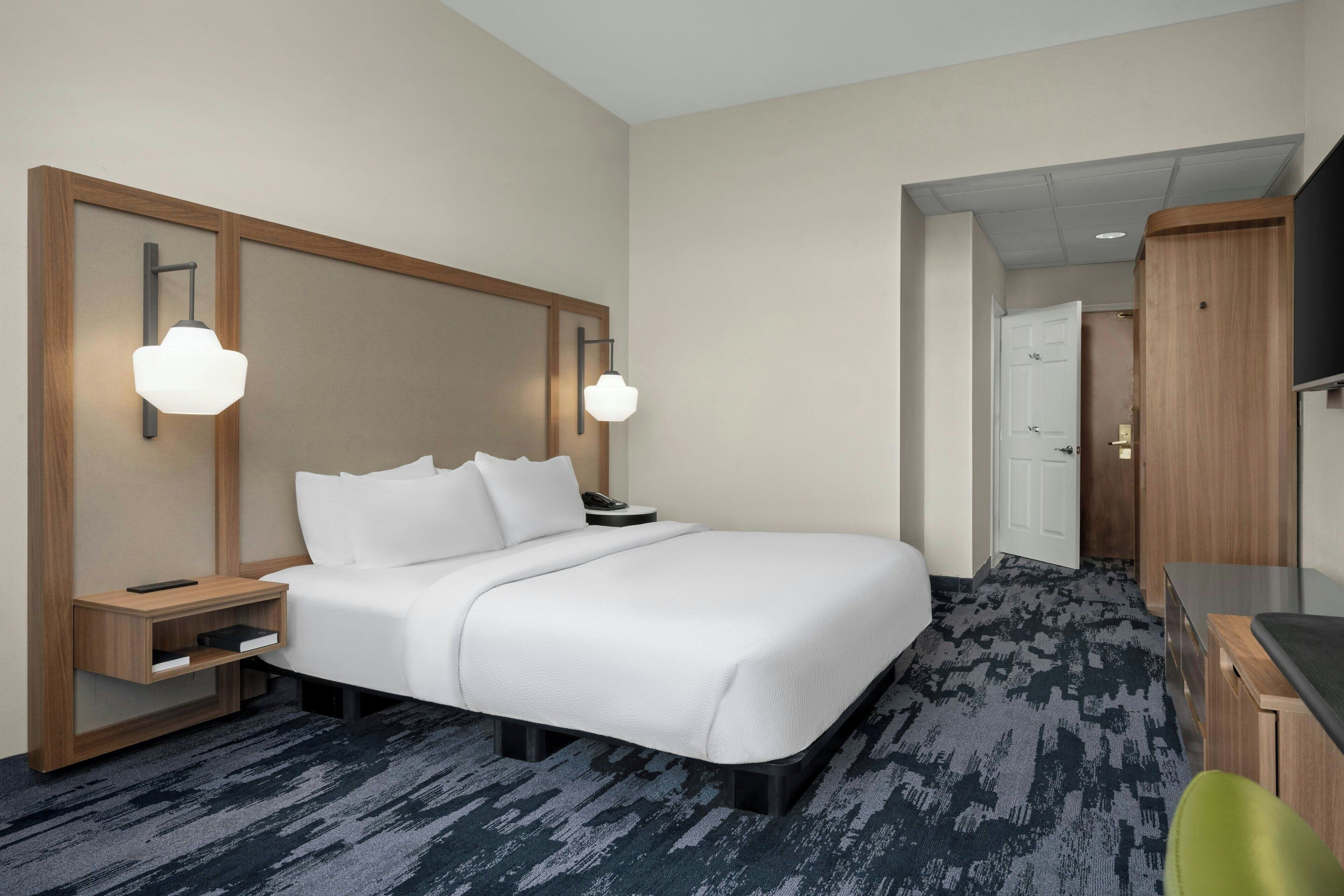 A hotel room with a large bed, bedside tables, a desk, and a television.