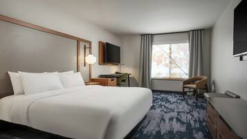 A hotel room with a large bed, a desk, a chair, a TV, and a window with curtains.