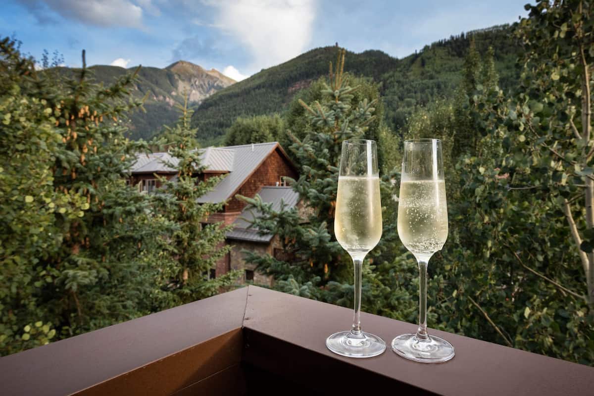 Two champagne flutes on a balcony with a mountainous landscape in the background.