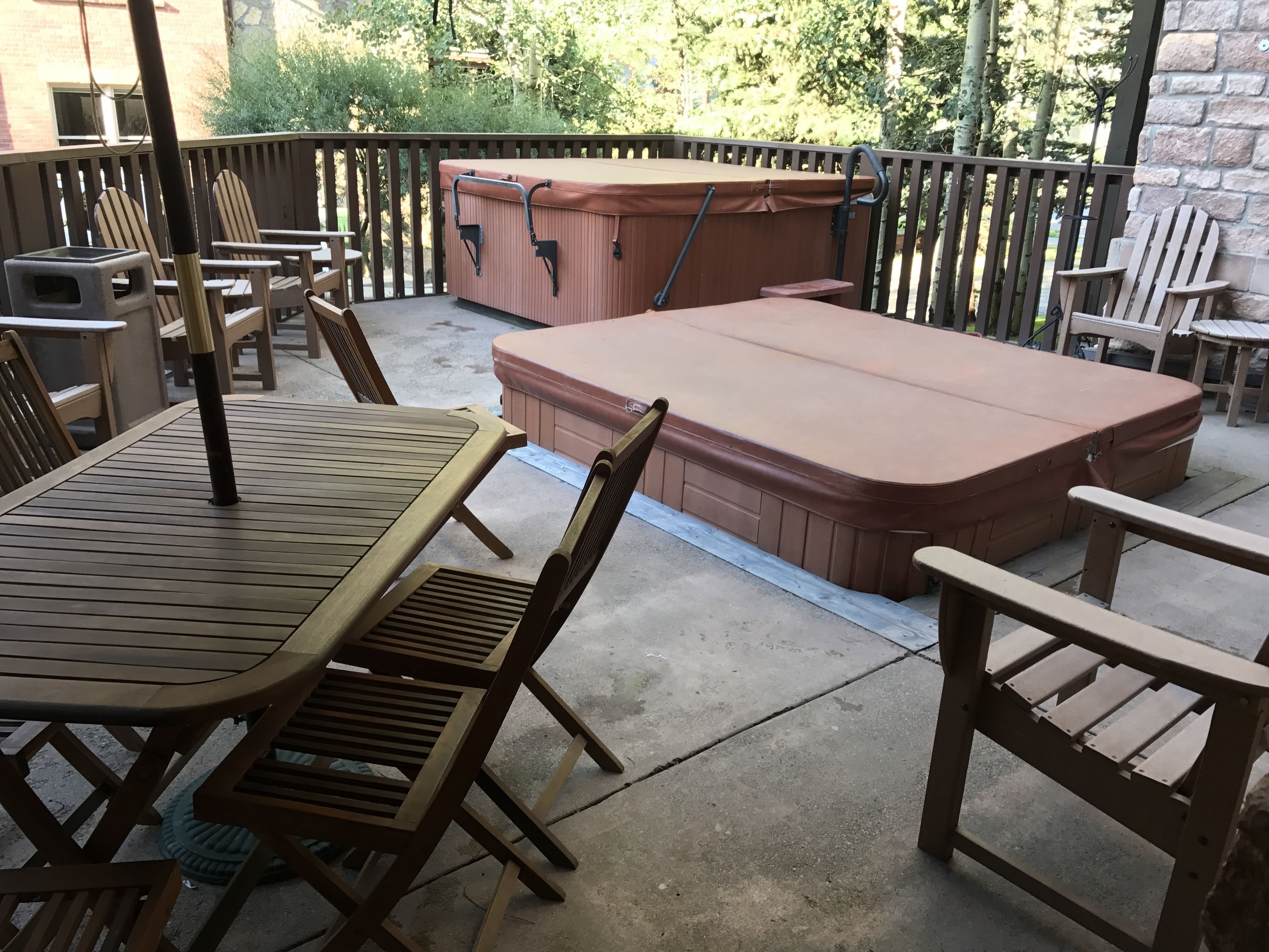 An outdoor patio with a wooden table, chairs, and a hot tub.