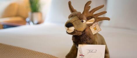 A plush toy deer on a bed with a hotel card and a small gift box.
