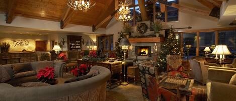 A cozy, well-lit living room with a fireplace, plush seating, and a Christmas tree.