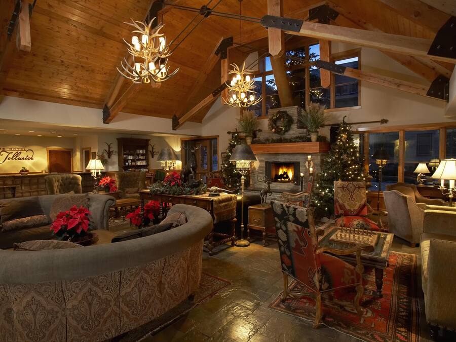 A cozy, well-lit living room with a fireplace, plush seating, and a Christmas tree.