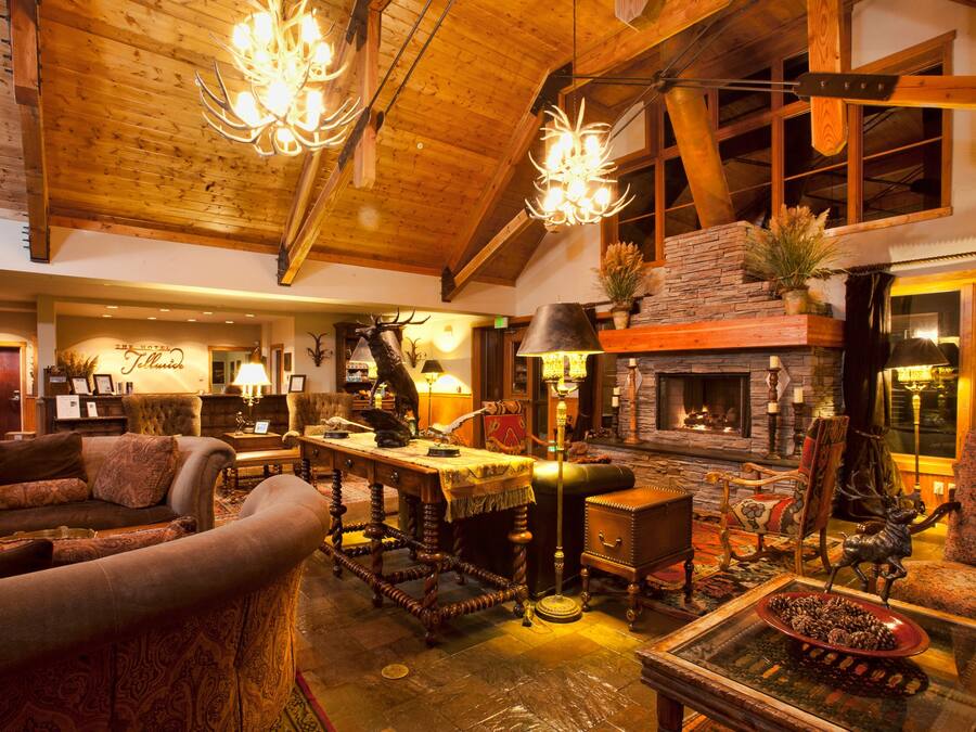 Un acogedor vestíbulo de hotel con chimenea, techo de madera y decoración rústica que incluye astas de ciervo y una estatua de venado.