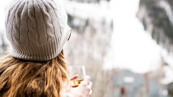 Una persona de cabello largo con un gorro blanco de punto y un suéter blanco, sentada junto a una ventana con vistas a un paisaje nevado.