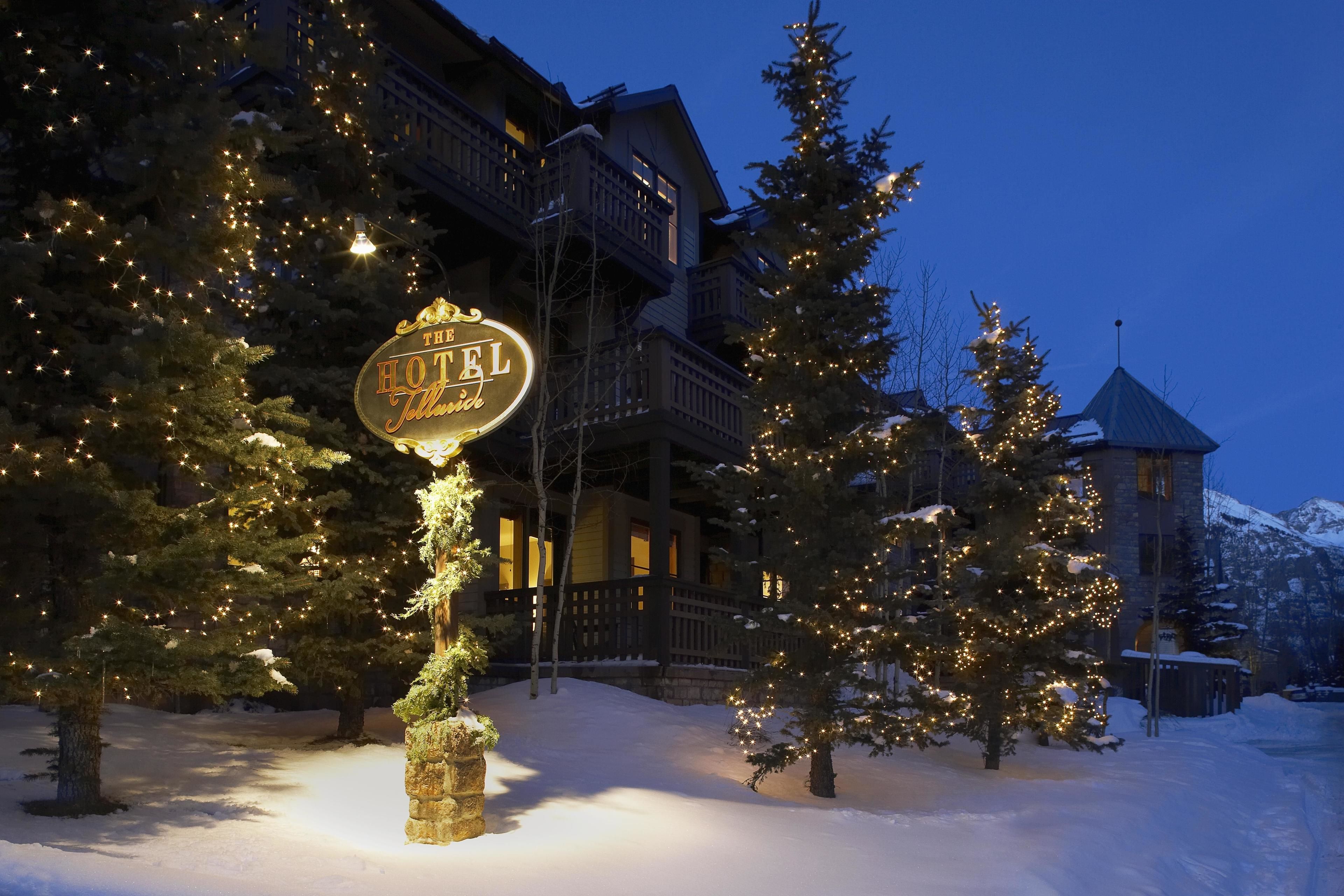 A snow-covered landscape with a lit sign for "The Hotel Jyllested" and snow-covered trees.