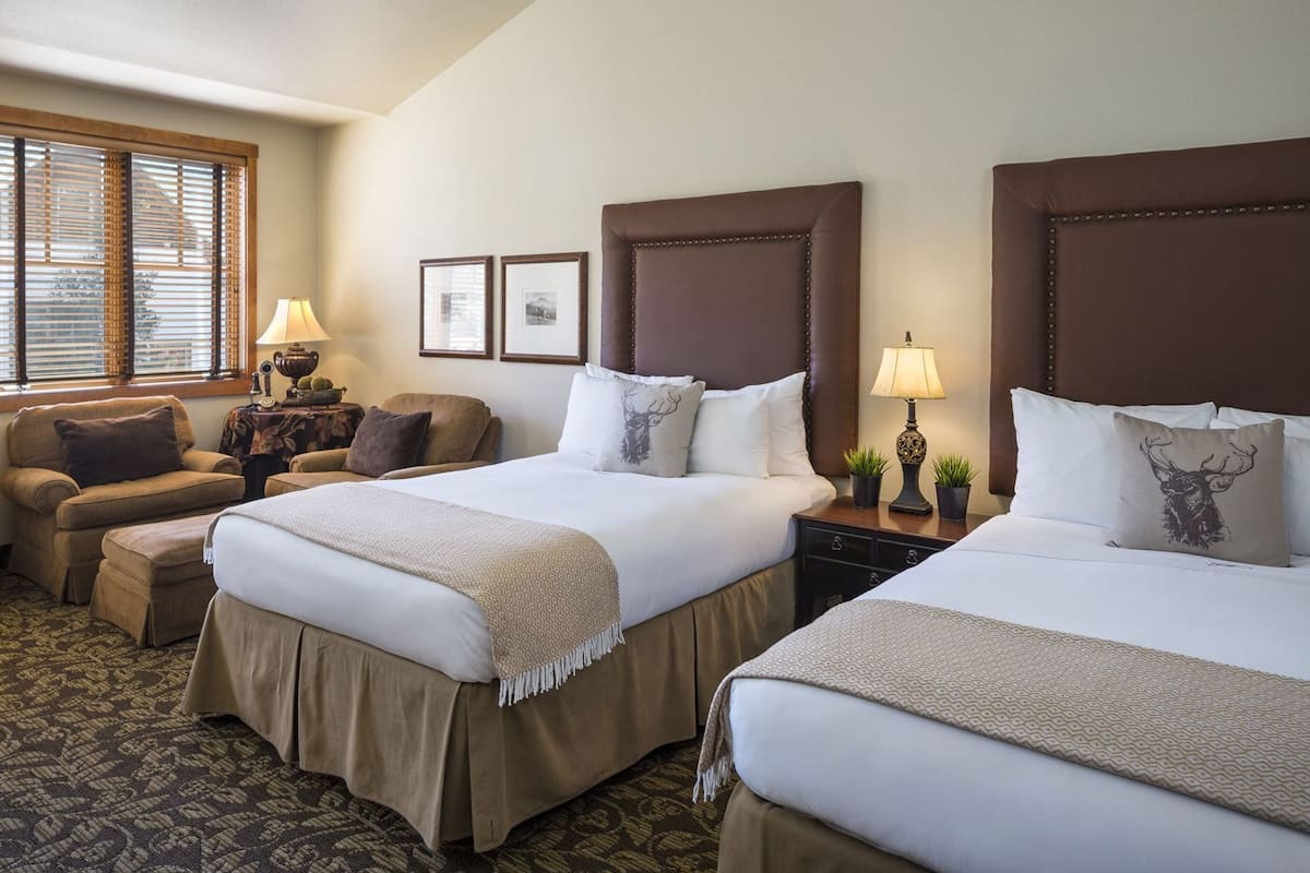 A hotel room with two beds, a sofa, a nightstand, and a window with blinds.