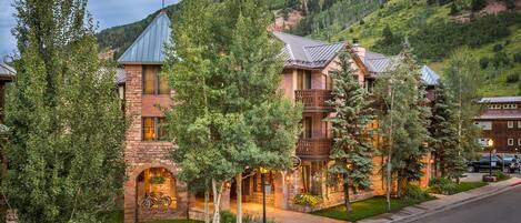 A multi-story hotel with a stone facade, balconies, and a mountain backdrop.