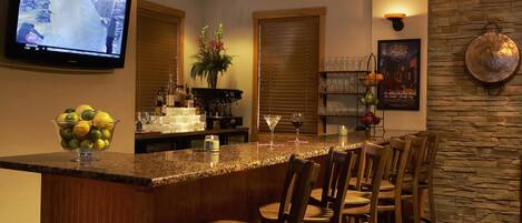 A bar area with a granite countertop, bar stools, a television, a potted plant, and a wine rack.