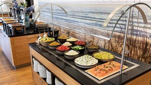 A buffet with various food items and a view of the ocean through a glass enclosure. - NH Zandvoort (Zandvoort)