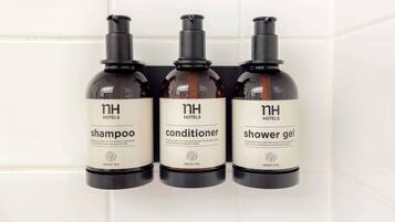 Tre flaconi di articoli da toilette dell'hotel: shampoo, balsamo e gel doccia, con l'etichetta 'NH Hotels' e 'TÈ VERDE'.