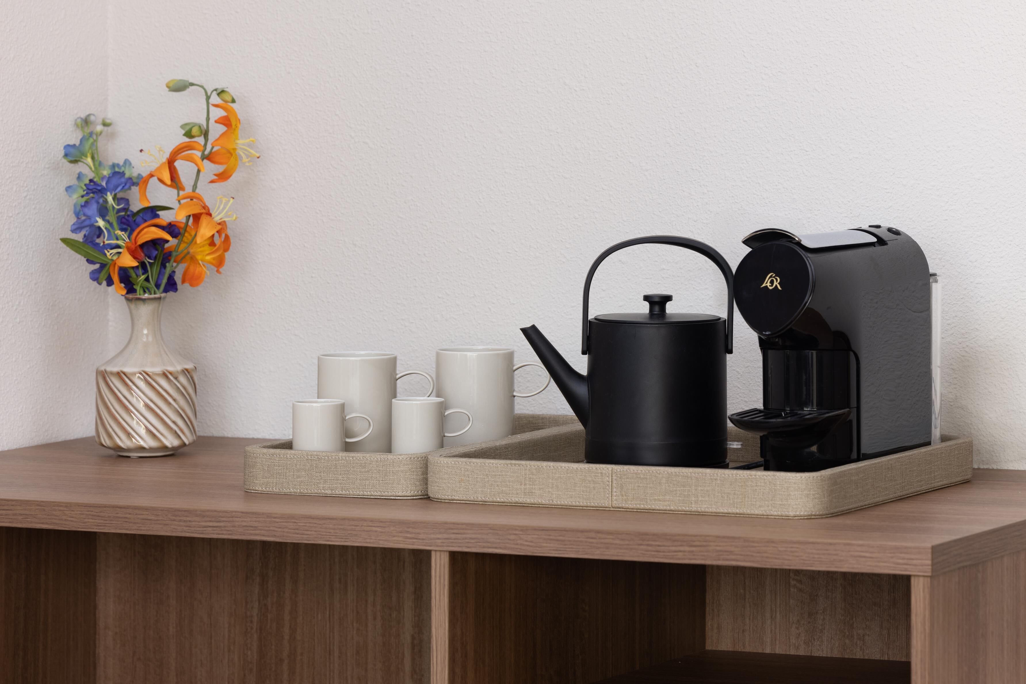 A wooden table with a vase of flowers, a kettle, and a coffee maker.