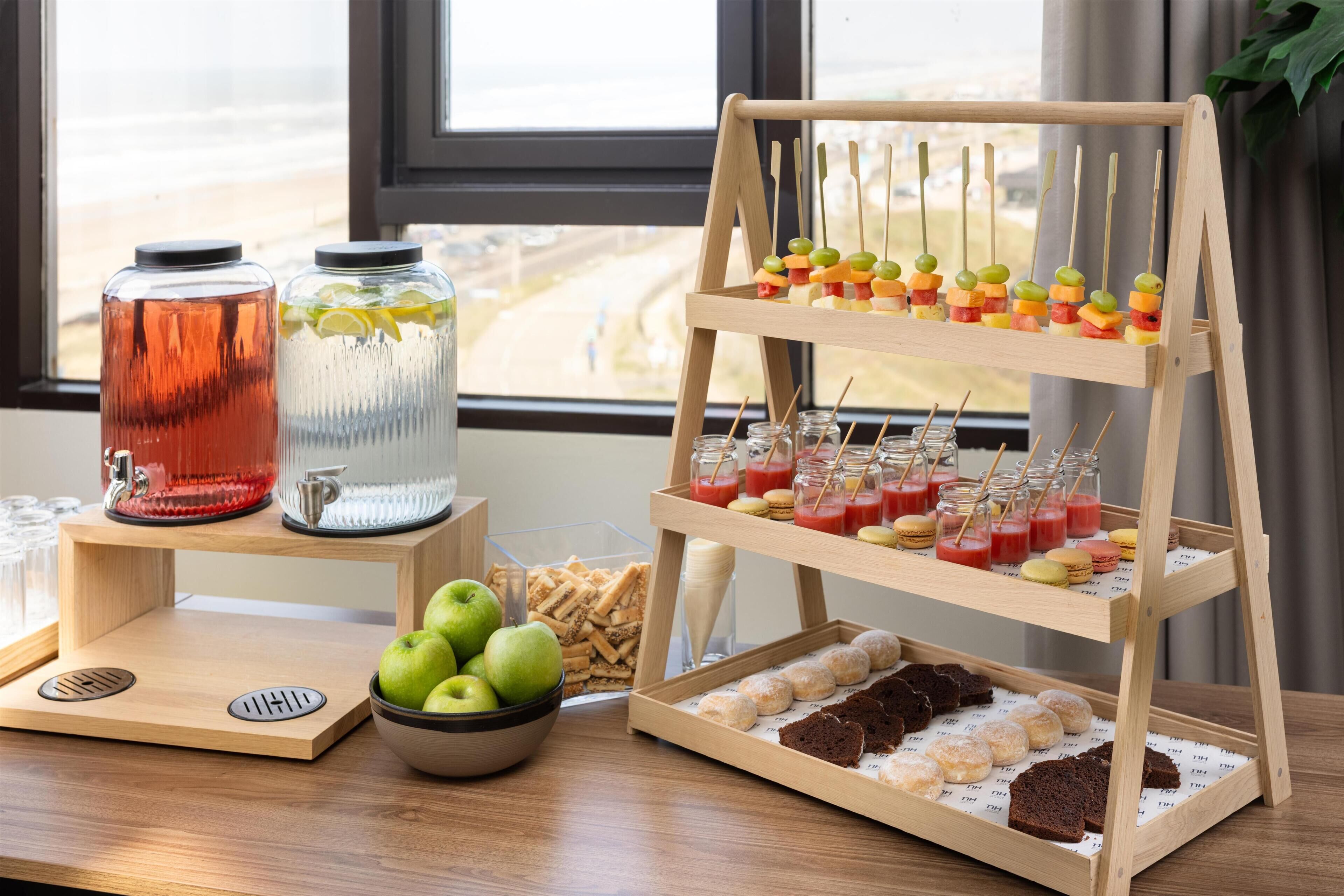 A wooden stand with snacks, a bowl of apples, and two glass containers on a table.