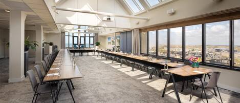 Un salón de conferencias con una larga mesa, sillas y grandes ventanales que ofrecen vistas de la ciudad.