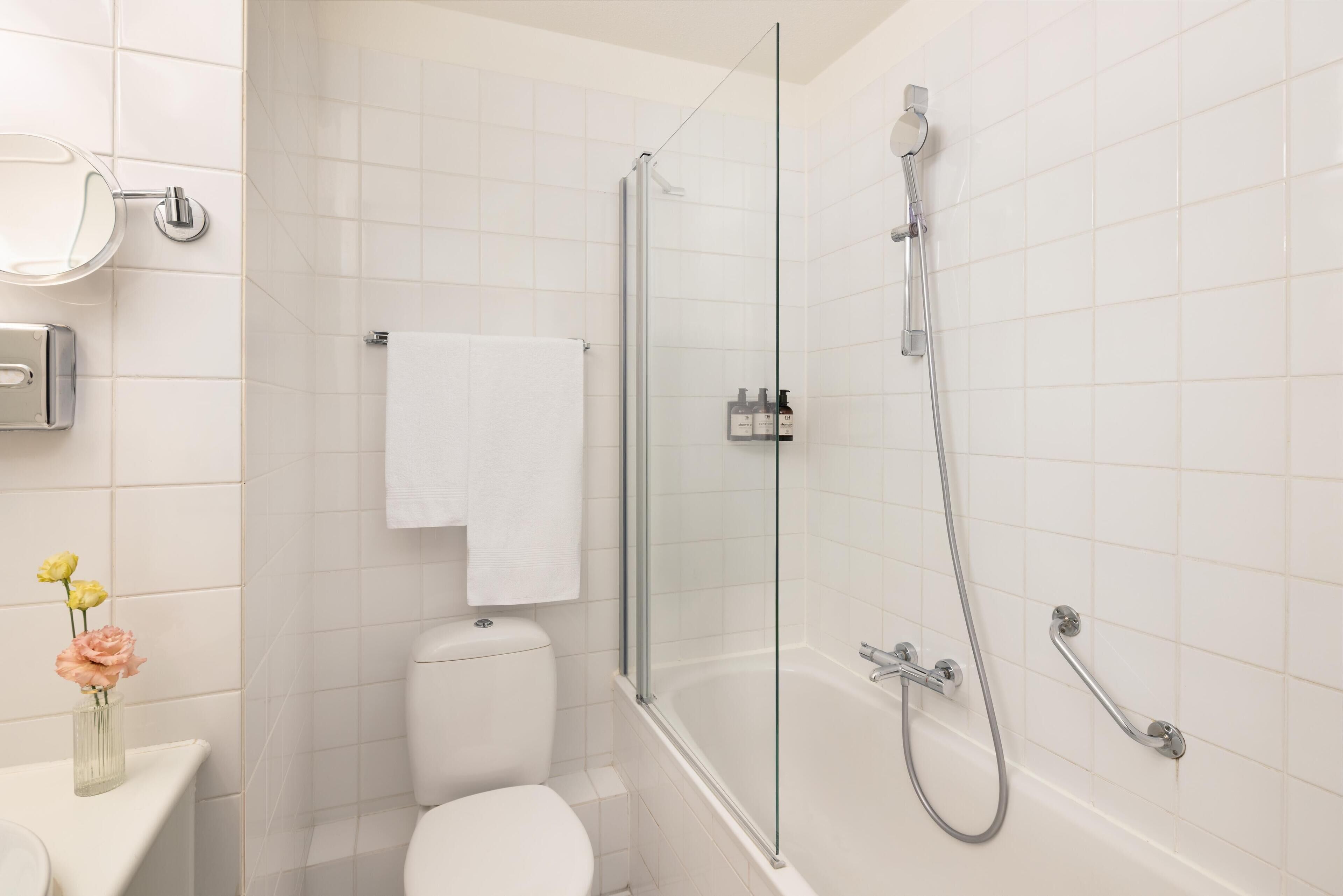 A modern bathroom with a glass-enclosed shower, a toilet, and a sink with a vase of flowers.