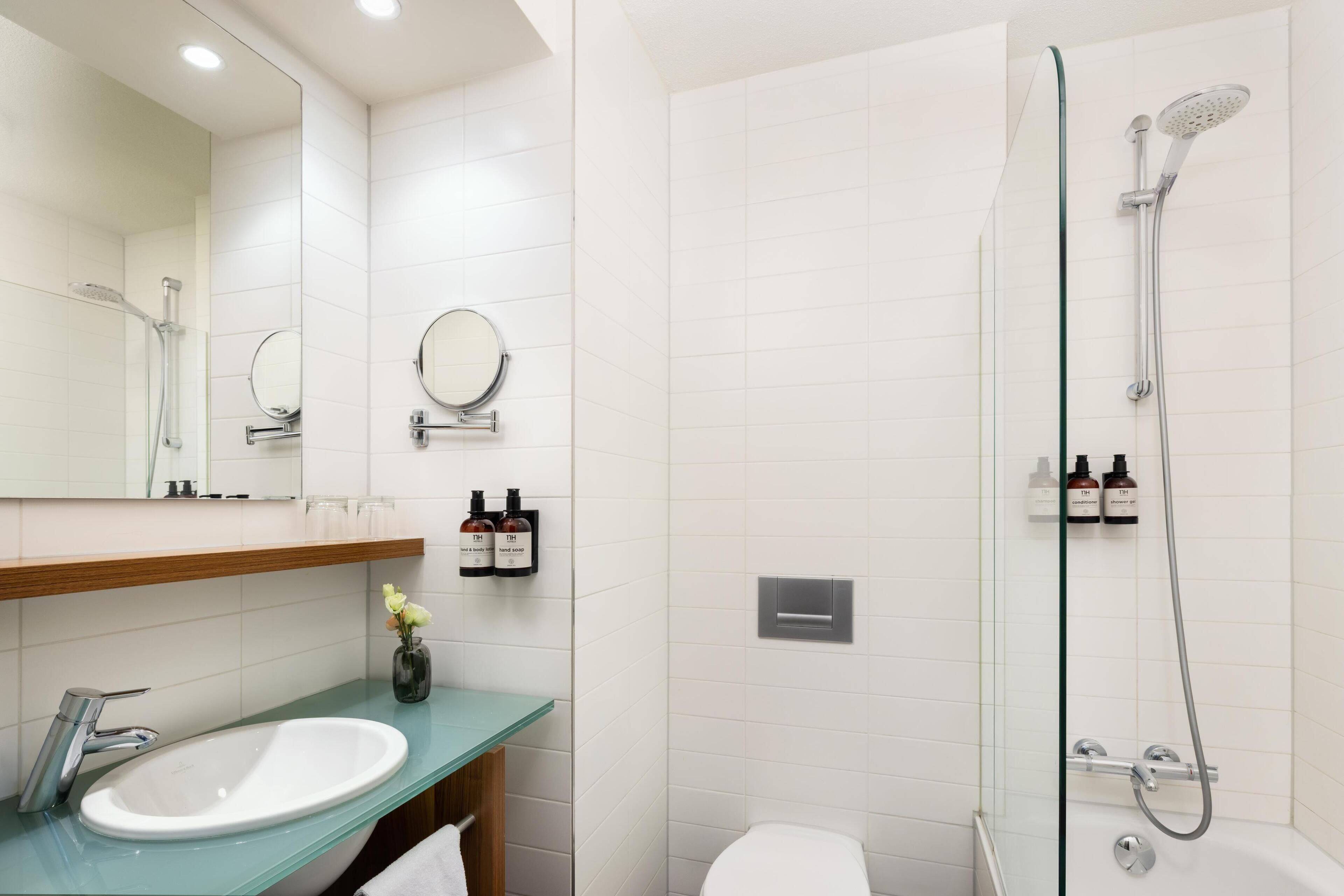 A modern bathroom with a glass shower enclosure, a white sink with a green countertop, and two round mirrors.